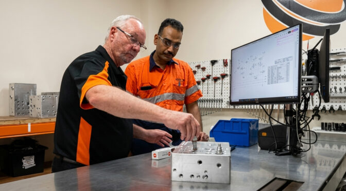 Two engineers assembling a custom hydraulic manifold in a precision workshop